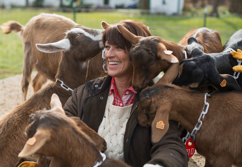 A farm sitter smiling among a herd of goats